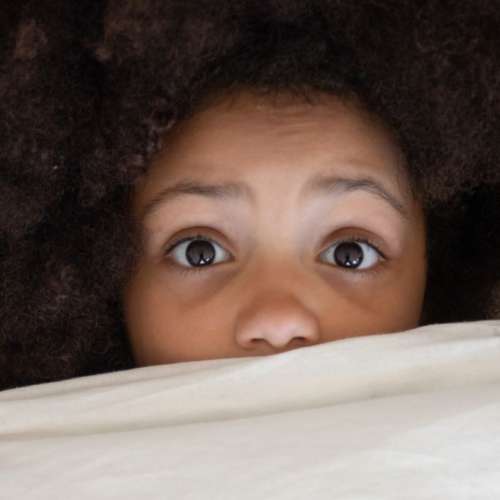 A child peeking over the bed covers.