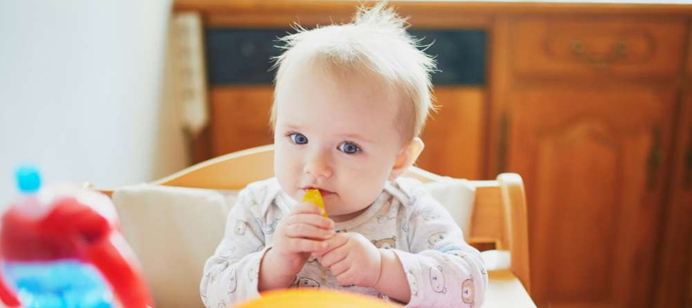 A teething 6 month old practicing baby led weaning with starter foods like peaches.