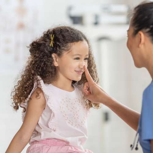 A child in the doctor's office, with a doctor looking at their nose.