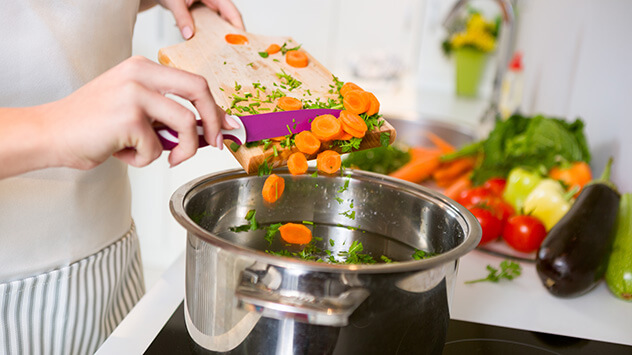Frau gibt geschnittenes Gemüse in den Suppentopf.