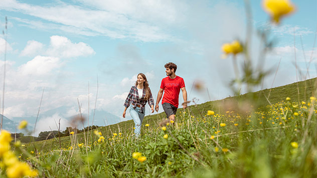 Paar wandert über Blumenwiese im Trentino