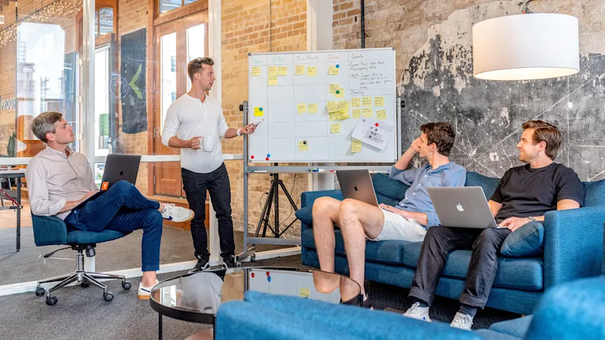 Image of several people meeting around a whiteboard to brainstorm and discuss topics from the board