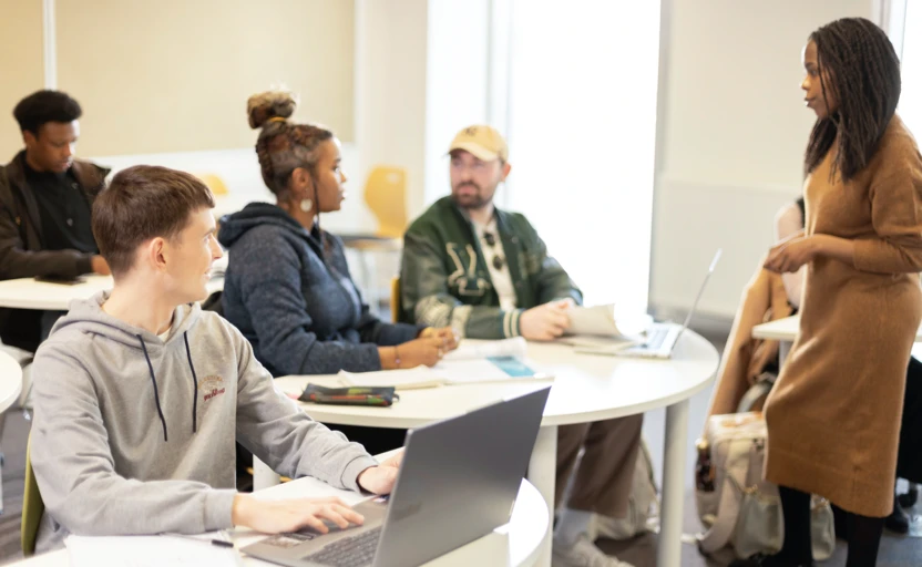 A group of young people sitting in a classroom setting while a lecturer chats with them.