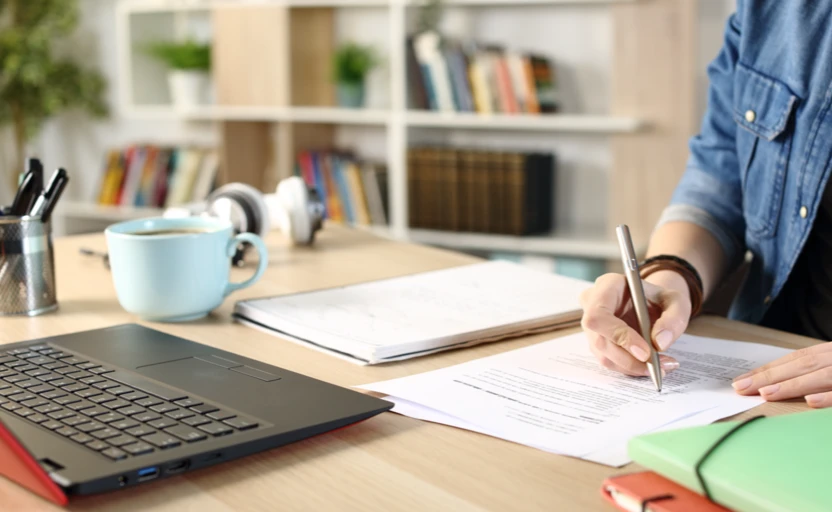 A person's hand holding a pen and writing on a sheet of paper.