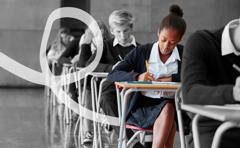 A group of school pupils sitting in a row at individual desks, they are working on test papers in front of them.