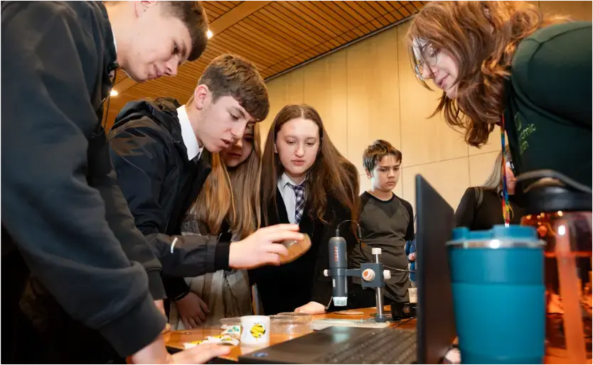 Three pupils take part in a table-top STEM activity while a teacher supervises from the other side of the table.