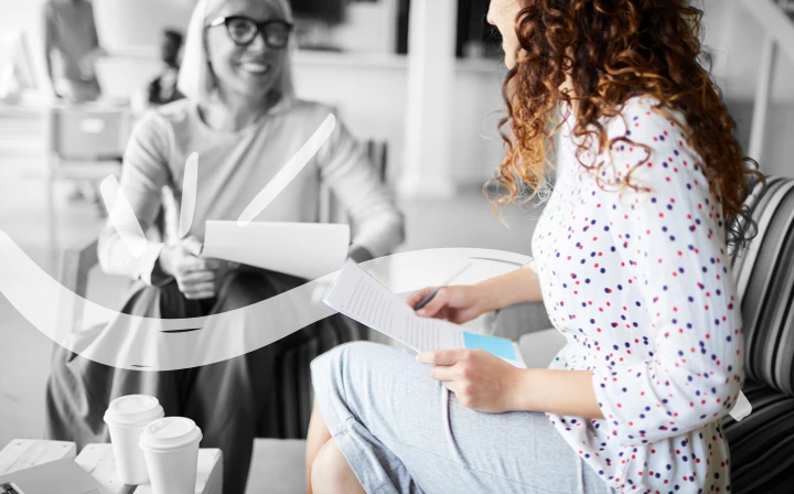Two people sitting having a coffee together, both are holding ther CVs and chatting.