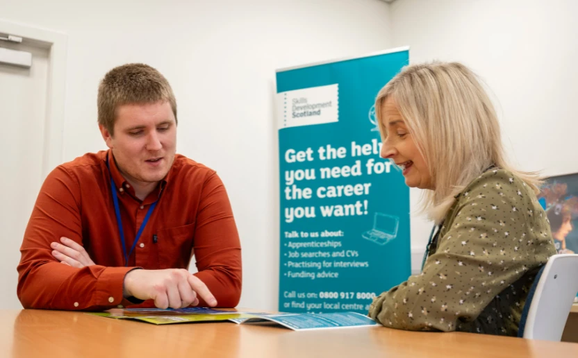A careers adviser chatting with a customer, they're both looking at a booklet and talking about it.