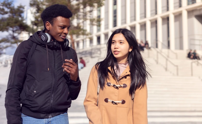 Two young people walking and talking outside of a college building.