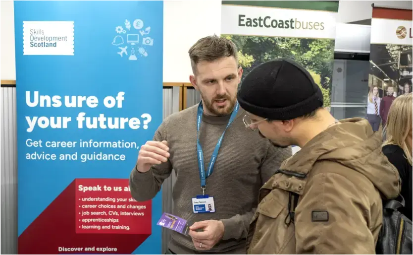Two men speak at a careers event. A sign in the background says 'Unsure of your future? Get career information, advice and guidance'.
