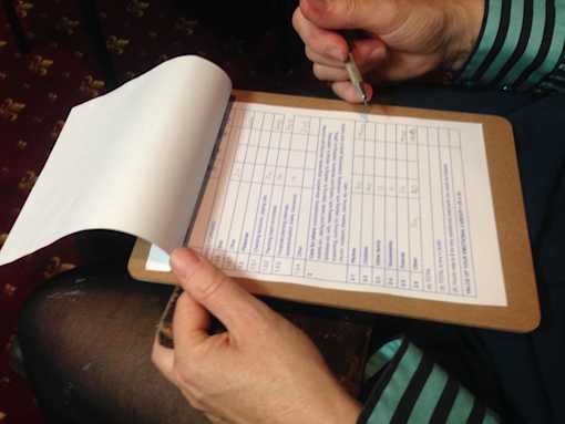 Note pad with paper containing a table, a person's hand seen writing on the paper