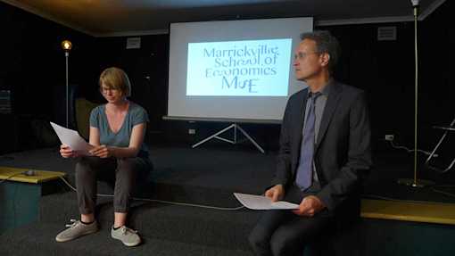 Two person sitting on stage in front of screen projecting the MSE logo