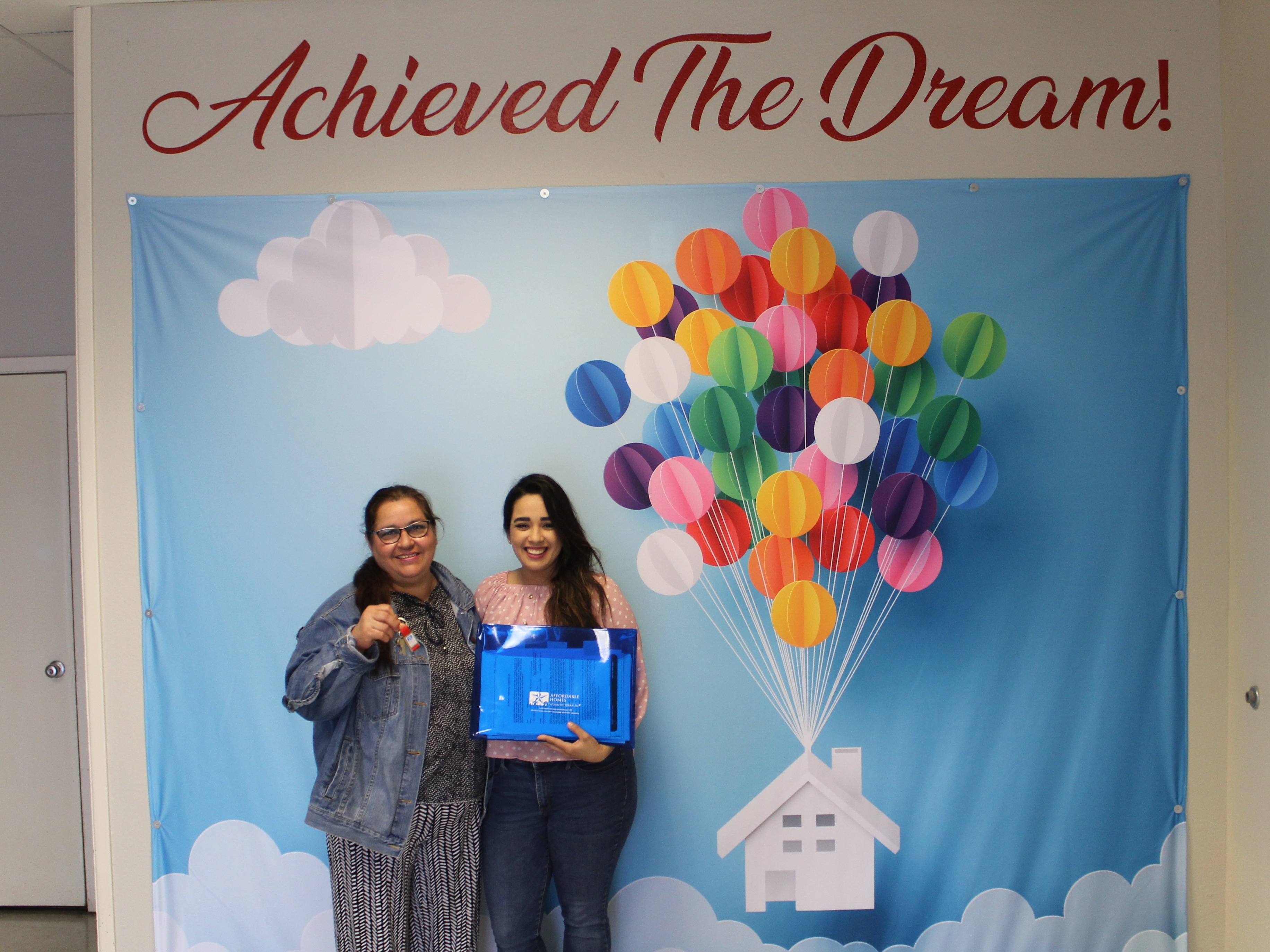 2 women standing in front of an Achieved The Dream background