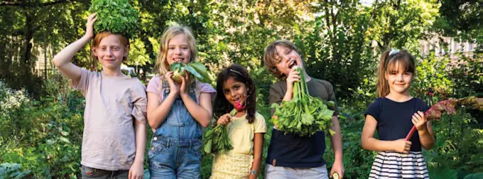 Kinder stehen in einem grünen Garten und halten Gemüsepflanzen in der Hand