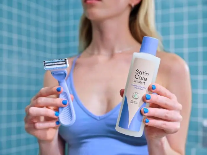 Frau präsentiert den Gillette Venus Intimate Rasierer und das Satin Care Intimpflege 2-in-1 Reinigungs- und Rasiergel für die sanfte Intimpflege und Rasur.