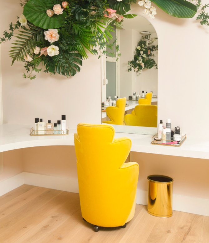 Long desk with mirror, bright yellow chair and jungle-like plants above.