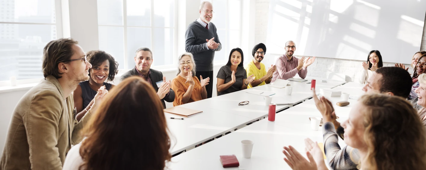 Photo of a group of people sitting around a room, clapping during a meeting