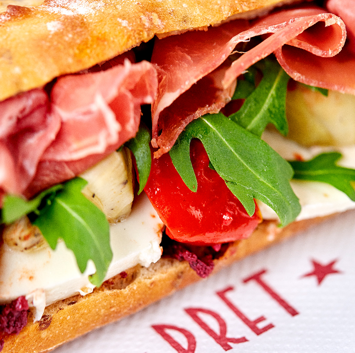 A close-up photograph of a prosciutto baguette on a Pret napkin.