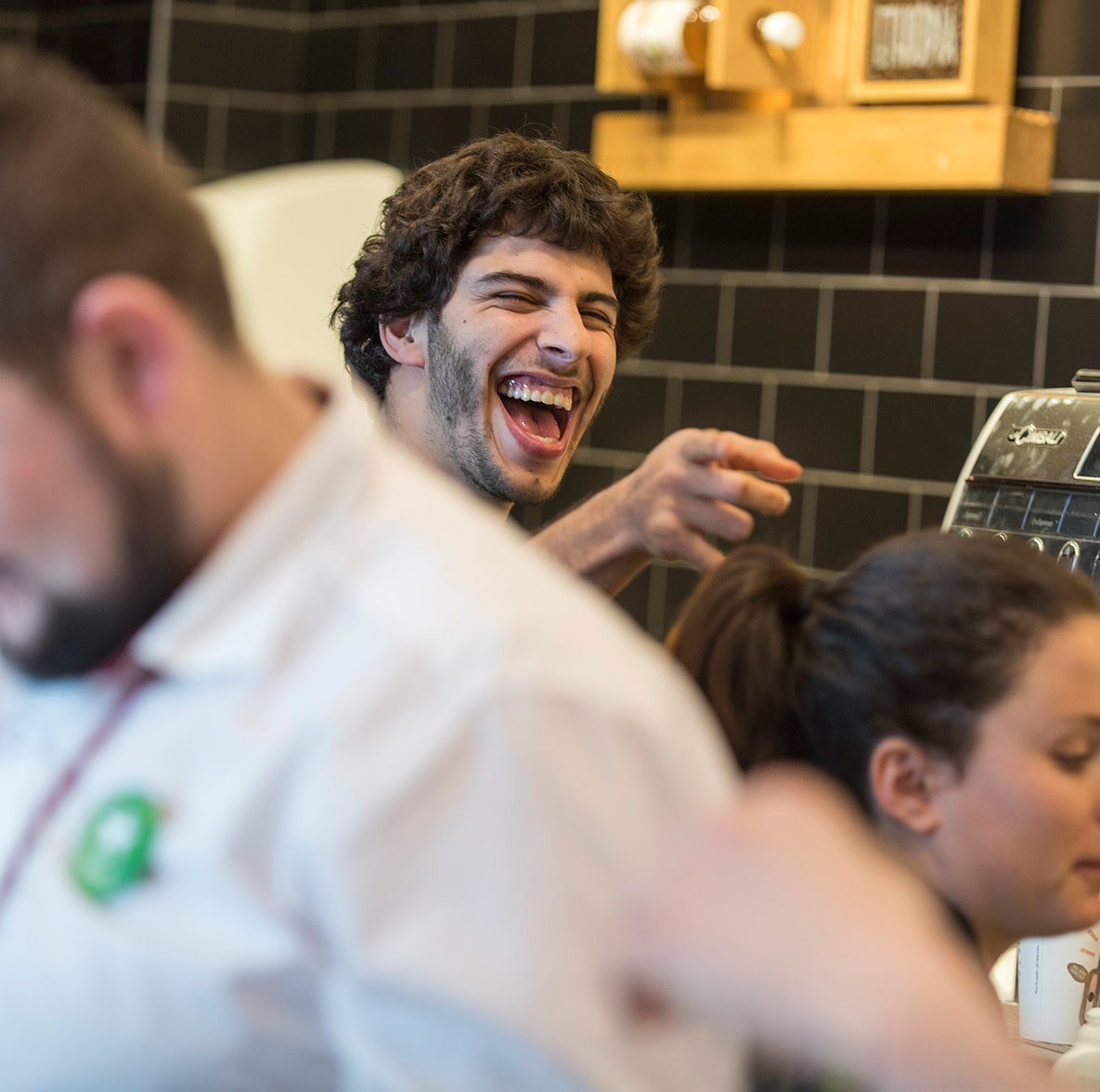 Team Member behind a till pointing towards the photographer and laughing