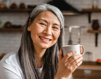 Lächelnde Frau mittleren Alters hält eine Tasse in der Hand