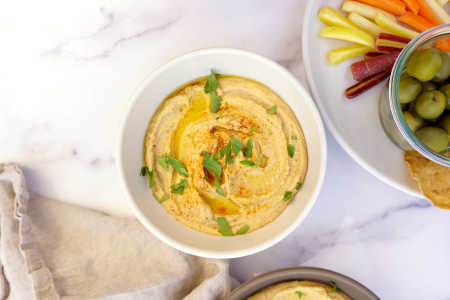 bowl of red lentil hummus with carrots, olives and pita chips
