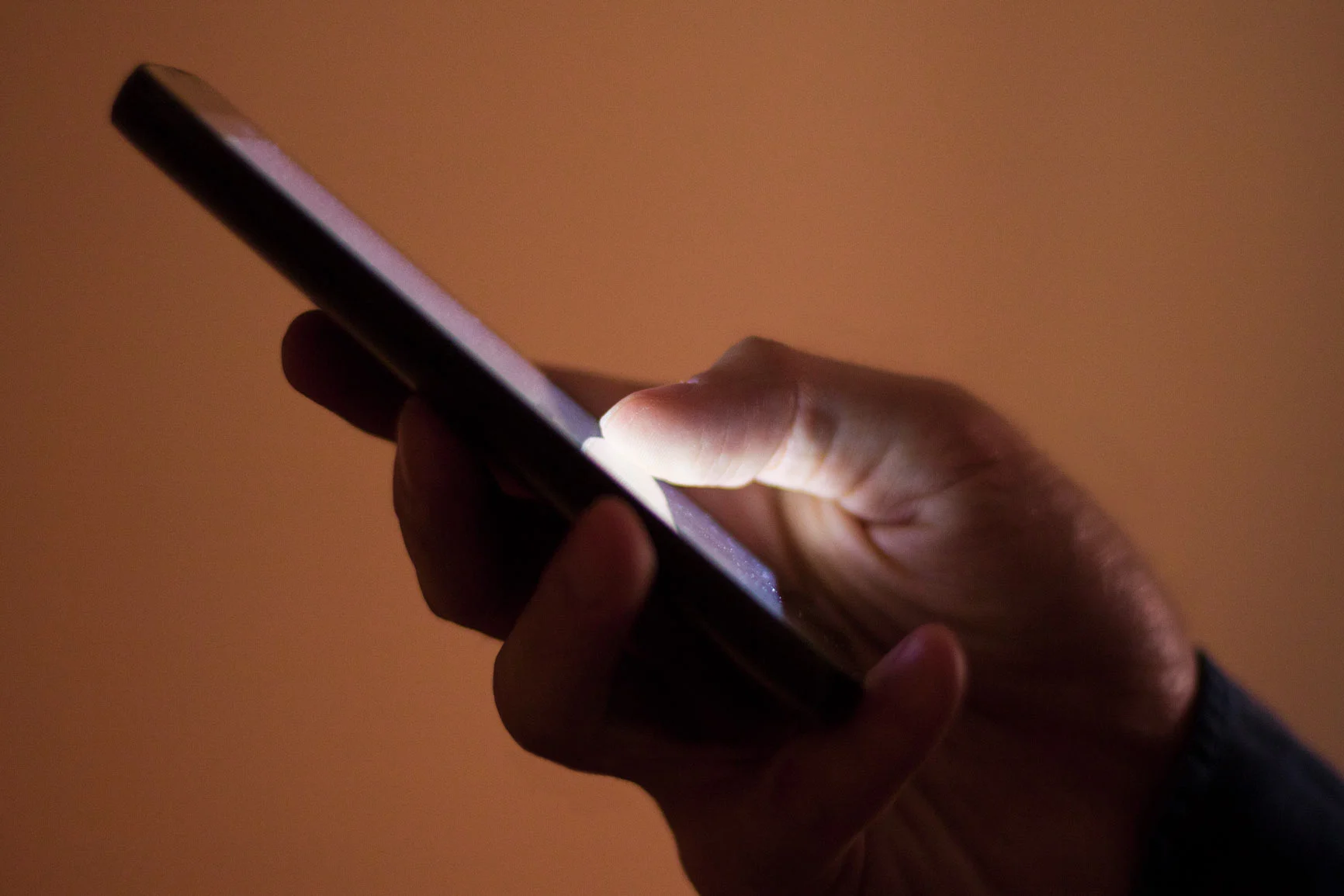 Hand hält Smartphone und tippt auf den Bildschirm in dunkler Umgebung. Hand hält Smartphone und tippt auf den Bildschirm in dunkler Umgebung.