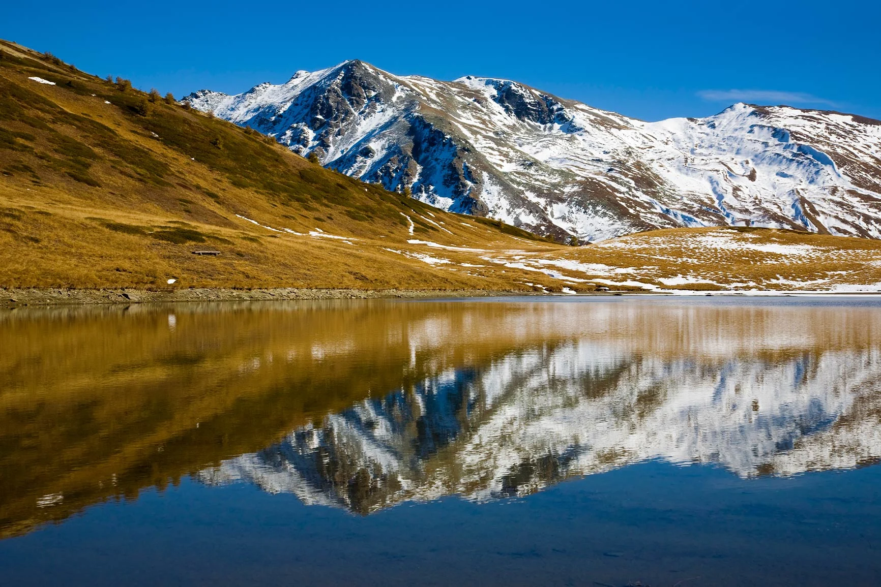 Reflection of snow-capped mountains Reflections of snow-capped mountains and grassy slopes on a tranquil mountain lake.