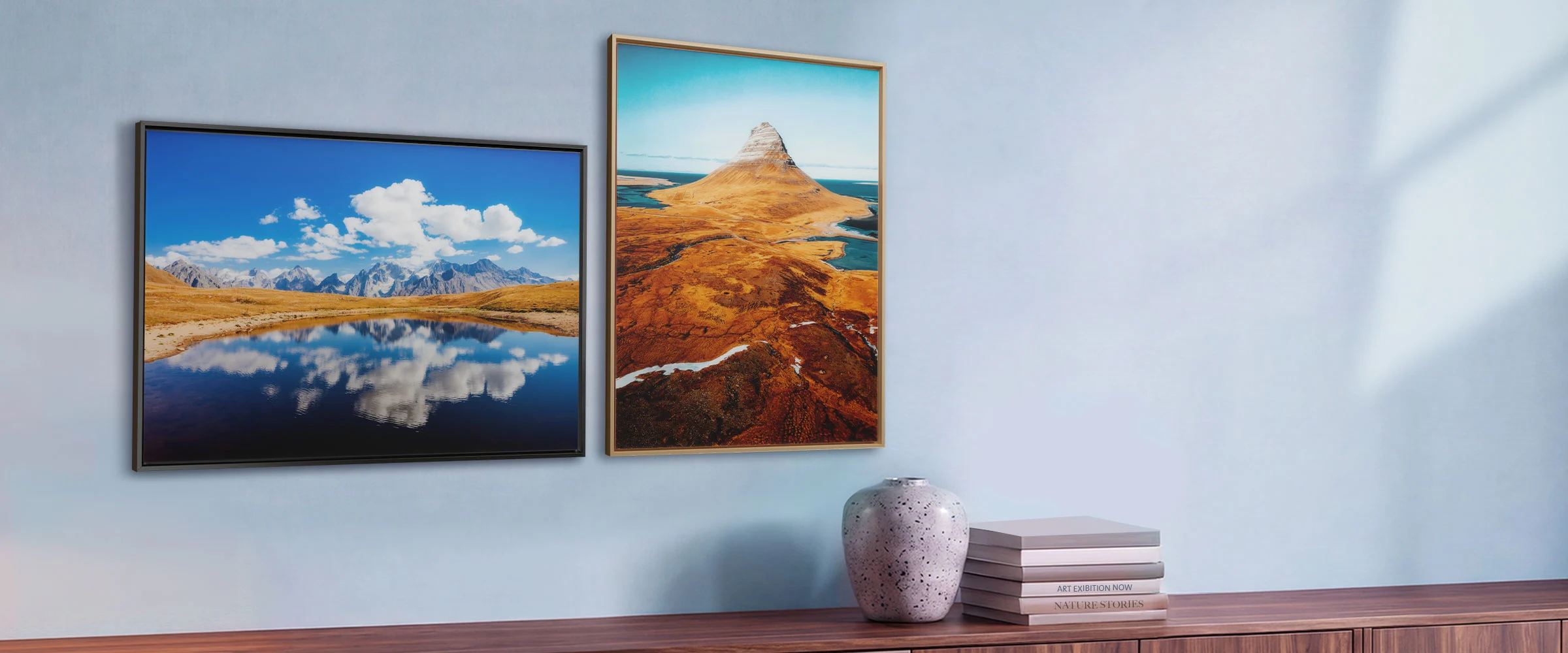 Zwei gerahmte Landschaftsdrucke an einer hellblauen Wand über einem Holz-Sideboard.