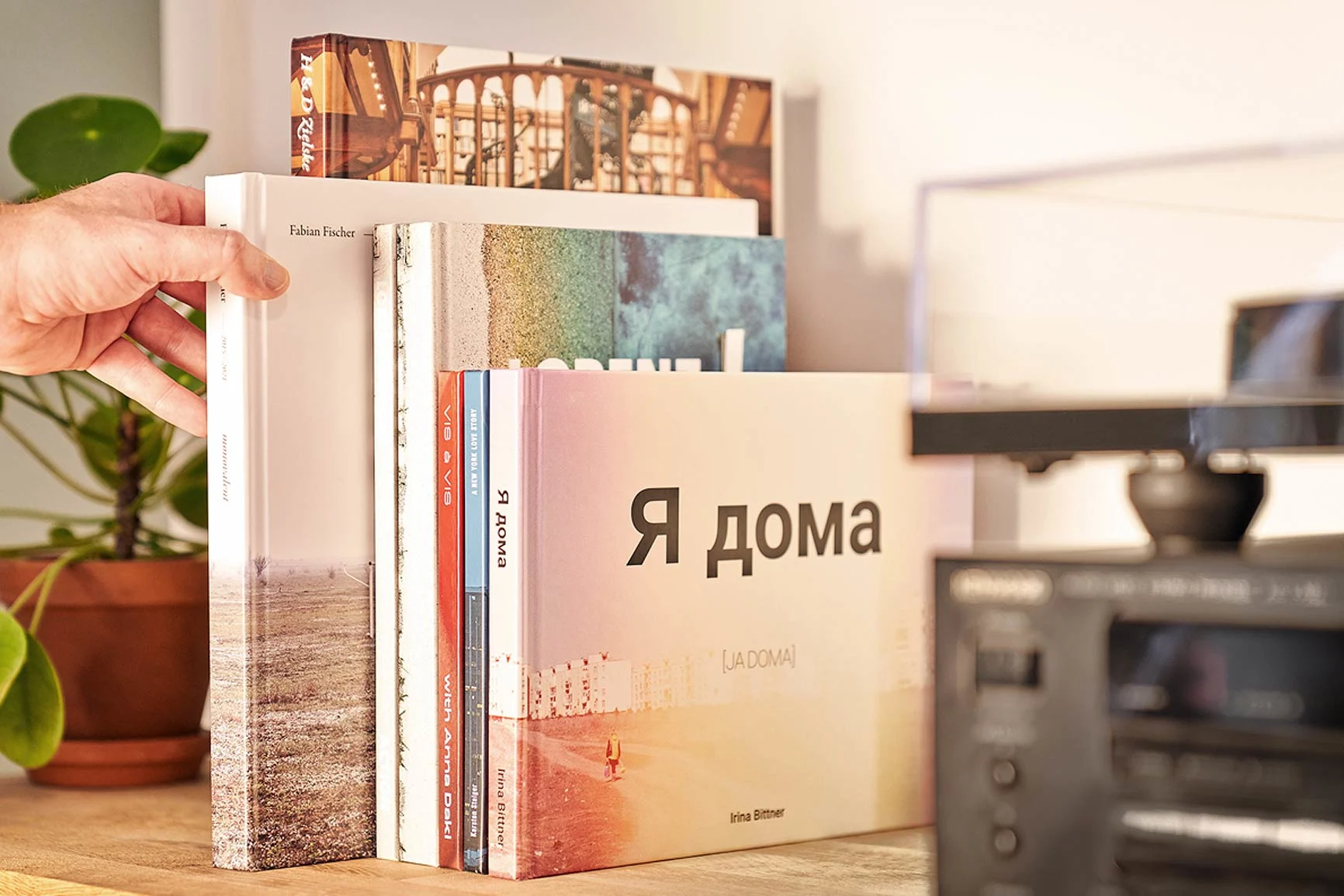 Hand pulls a book from a shelf with several coffee table books. Hand pulls a book from a shelf with several coffee table books.