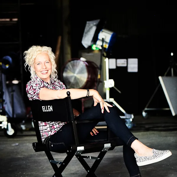 Portrait d'Ellen von Unwert L'artiste Ellen von Unwerth est assise, détendue, sur une chaise de réalisateur noire dans un studio équipé de lumières et de matériel.