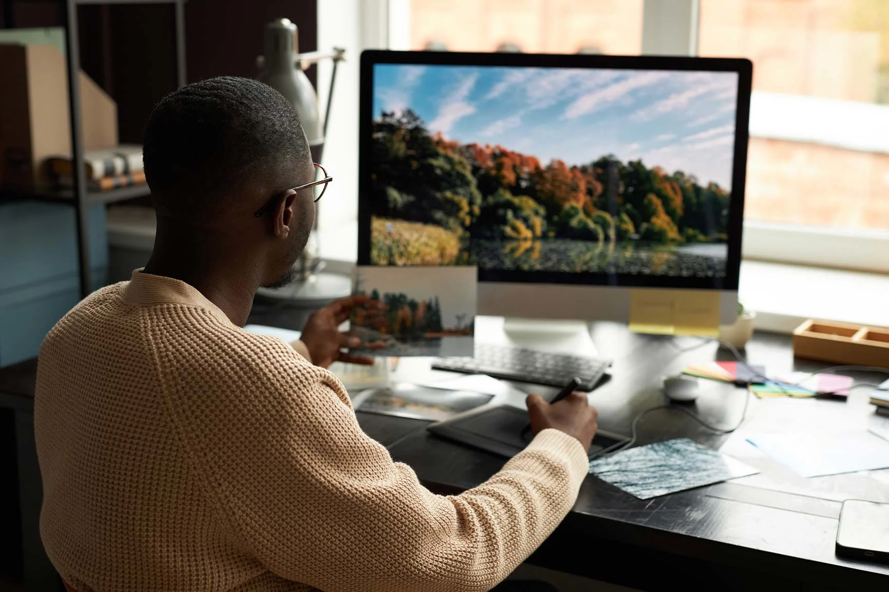 Un uomo è seduto alla scrivania e sta confrontando una foto sul computer con una stampa che ha in mano. Un uomo è seduto alla scrivania e sta confrontando una foto sul computer con una stampa che ha in mano.