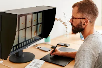 Classement & archivage des images 2 Un homme est assis à son bureau et modifie des images sur une tablette graphique tandis que l'écran les affiche.