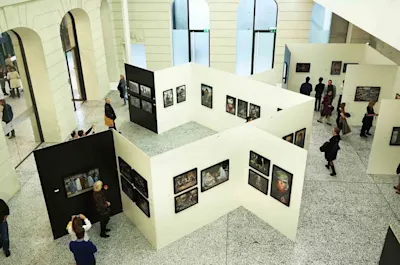 Berlin Foto Biennale Ausstellung Fotoausstellung mit weißen Trennwänden, gerahmten Bildern und Besuchern in heller Halle.
