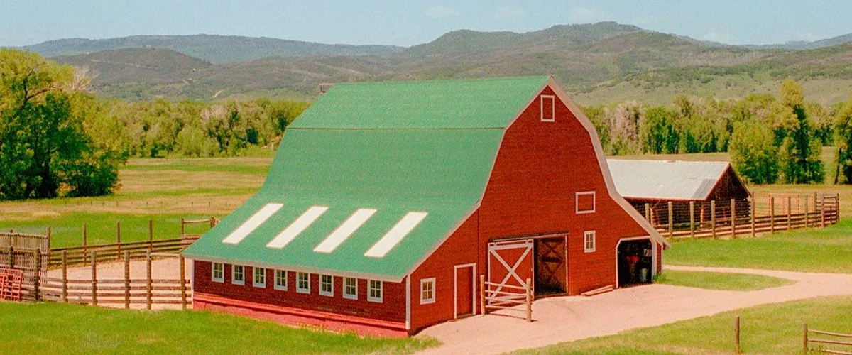 A red farmhouse with a green gabled roof in a meadow set against wooded hills.