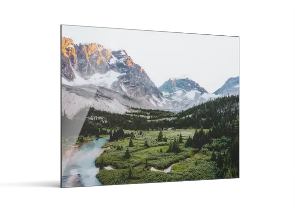 A metal print displaying a mountain landscape with snow-capped peaks, a green valley, evergreen trees, and a winding blue river.