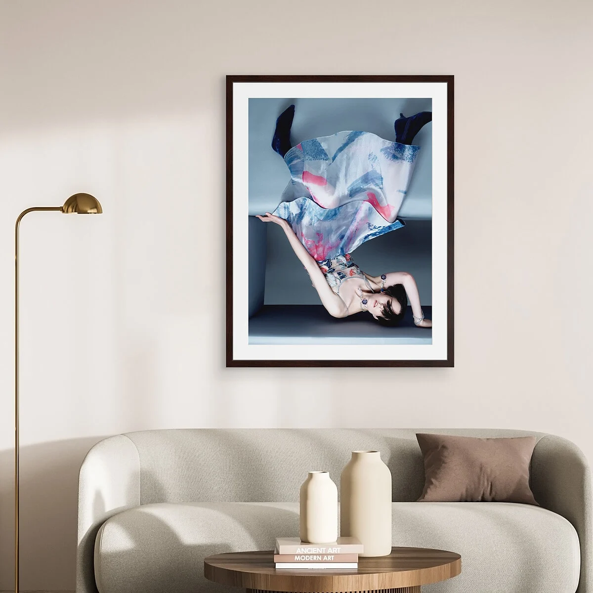 Modernes Wohnzimmer mit einem beigen Sofa, einer Messing-Stehlampe und einem Modefoto mit fließenden Stoffen in Blau und Rosa, gerahmt in einem Passepartout-Rahmen. Modernes Wohnzimmer mit einem beigen Sofa, einer Messing-Stehlampe und einem Modefoto mit fließenden Stoffen in Blau und Rosa, gerahmt in einem Passepartout-Rahmen.