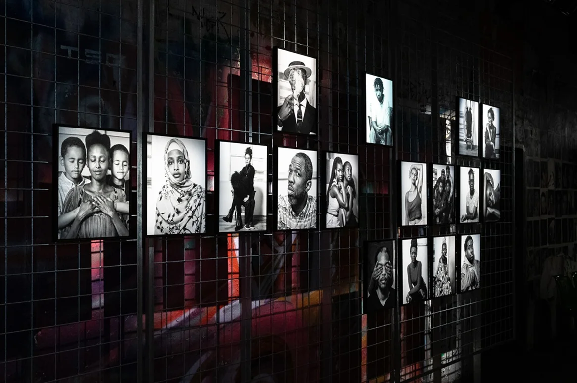 Exhibition _ Fotografiska_ Emerging Berlin Galerie-Wand mit schwarz-weißen Porträtfotografien, die in Reihen vor einem dunklen Hintergrund mit dezenter roter Beleuchtung angeordnet sind