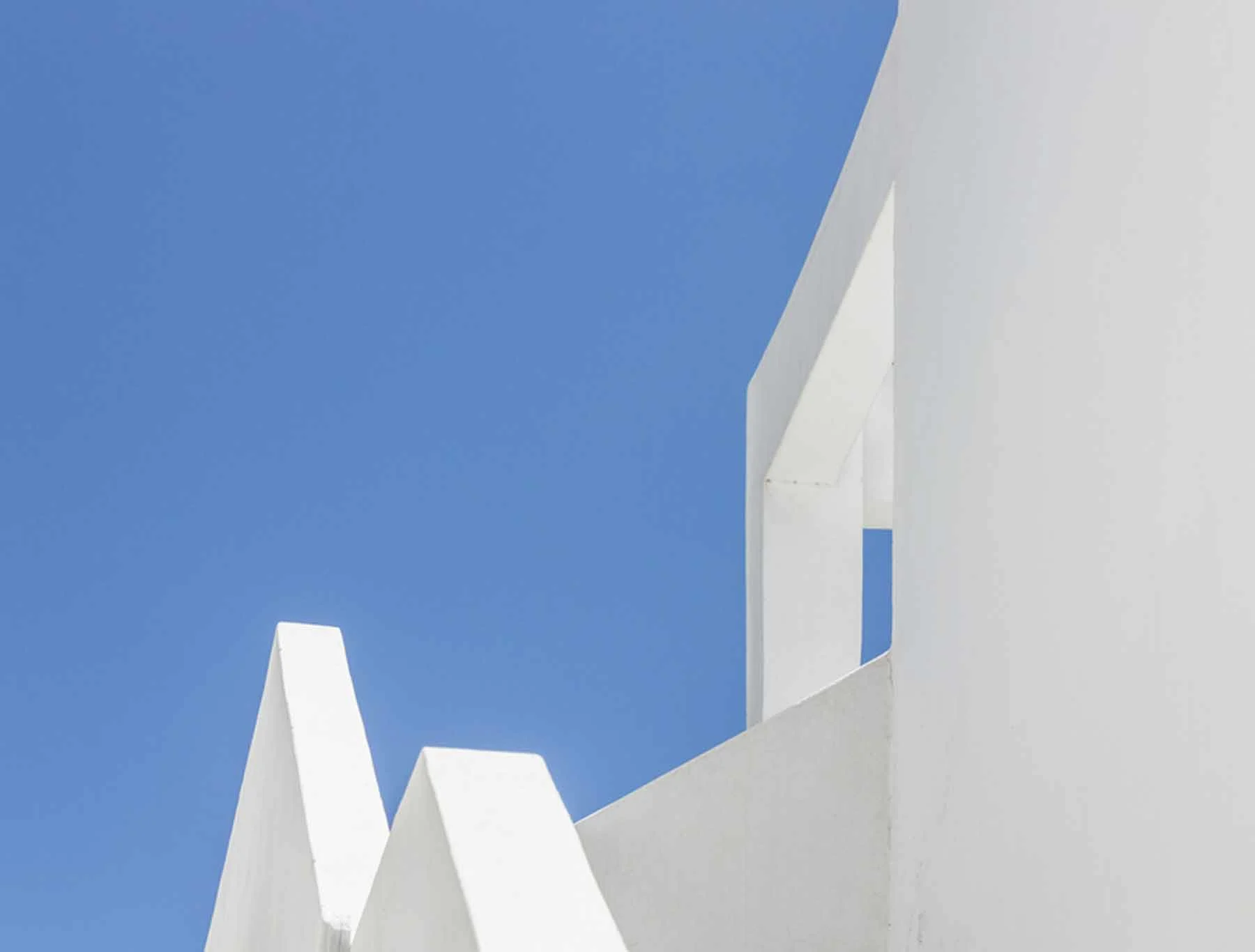 Formas geométricas blancas de edificios contra un cielo azul claro, arquitectura minimalista. Formas geométricas blancas de edificios contra un cielo azul claro, arquitectura minimalista.