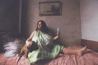 WhiteWall - Partner von Circulation(s) Portrait of a woman sitting with her dog on her bed holding her mobile phone in her hand.
