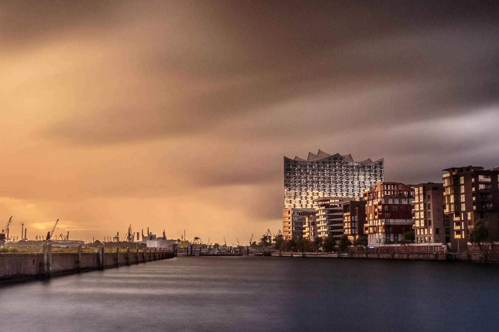 Elbphilharmonie and port facilities A view of the Elbphilharmonie and the harbor facilities under cloudy skies and calm waters.