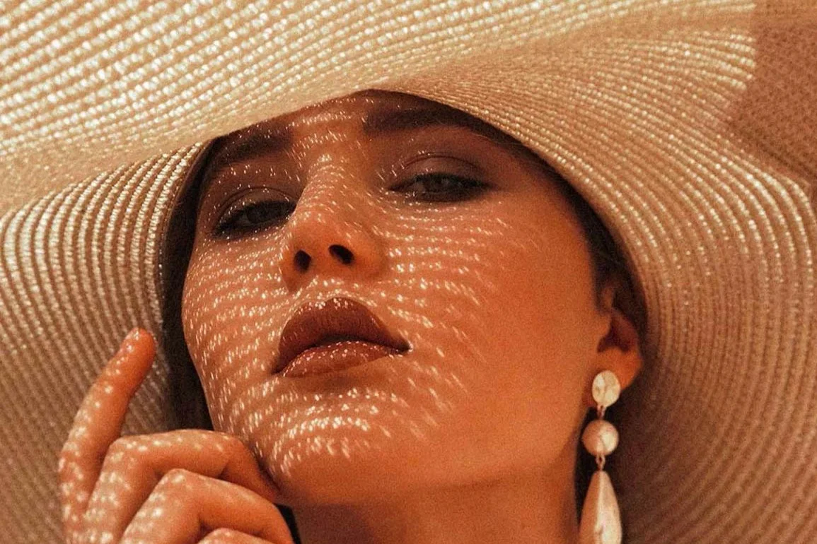 Portrait of a woman with a sun hat Portrait of a woman wearing a large sun hat and earrings, with one hand cupped to her face.