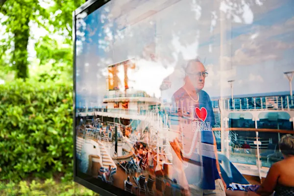 Outdoor exhibition showing a photo of a cruise ship deck with blue lounge chairs and "I Love Hawaii" sign