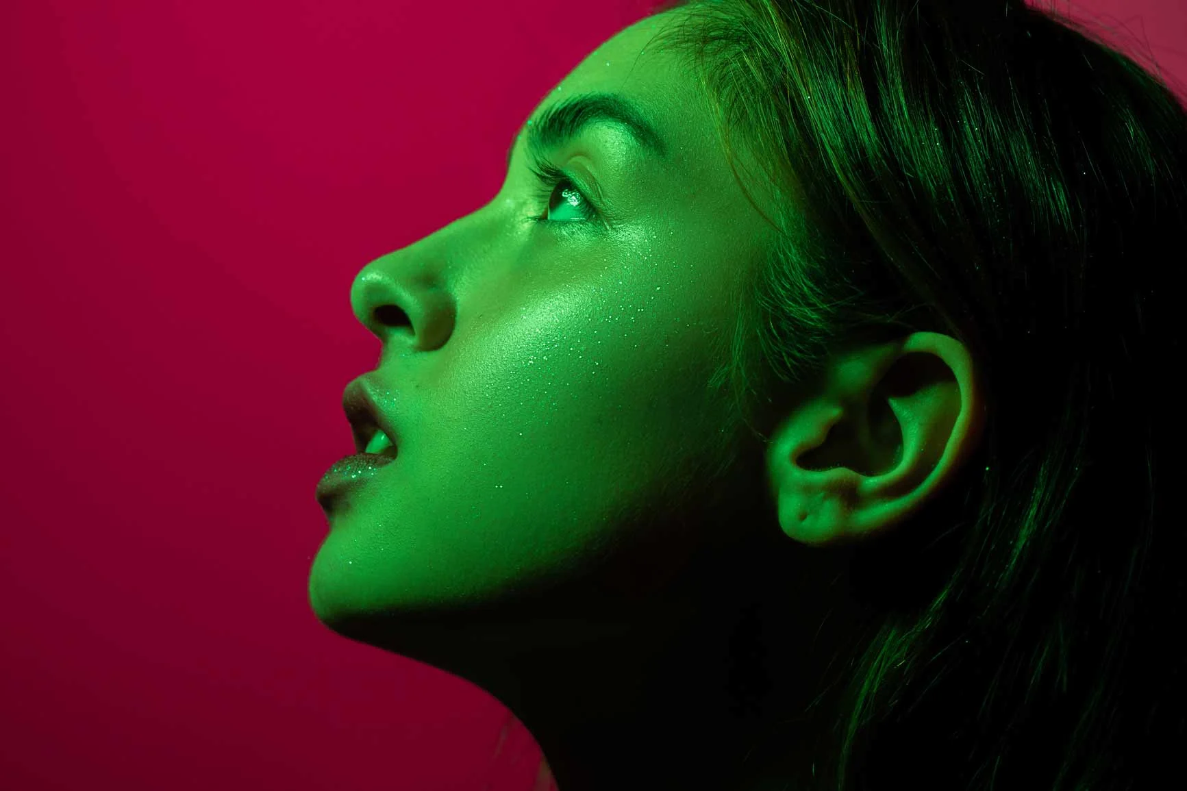 Retrato de una mujer joven de perfil, iluminación verde, fondo rojo, piel brillante. Retrato de una mujer joven de perfil, iluminación verde, fondo rojo, piel brillante.