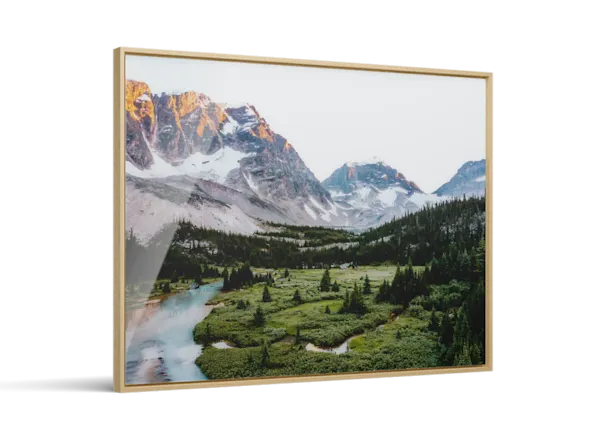 Framed landscape photo print showing snow-capped mountains, a winding turquoise river, and green pine forest valley.