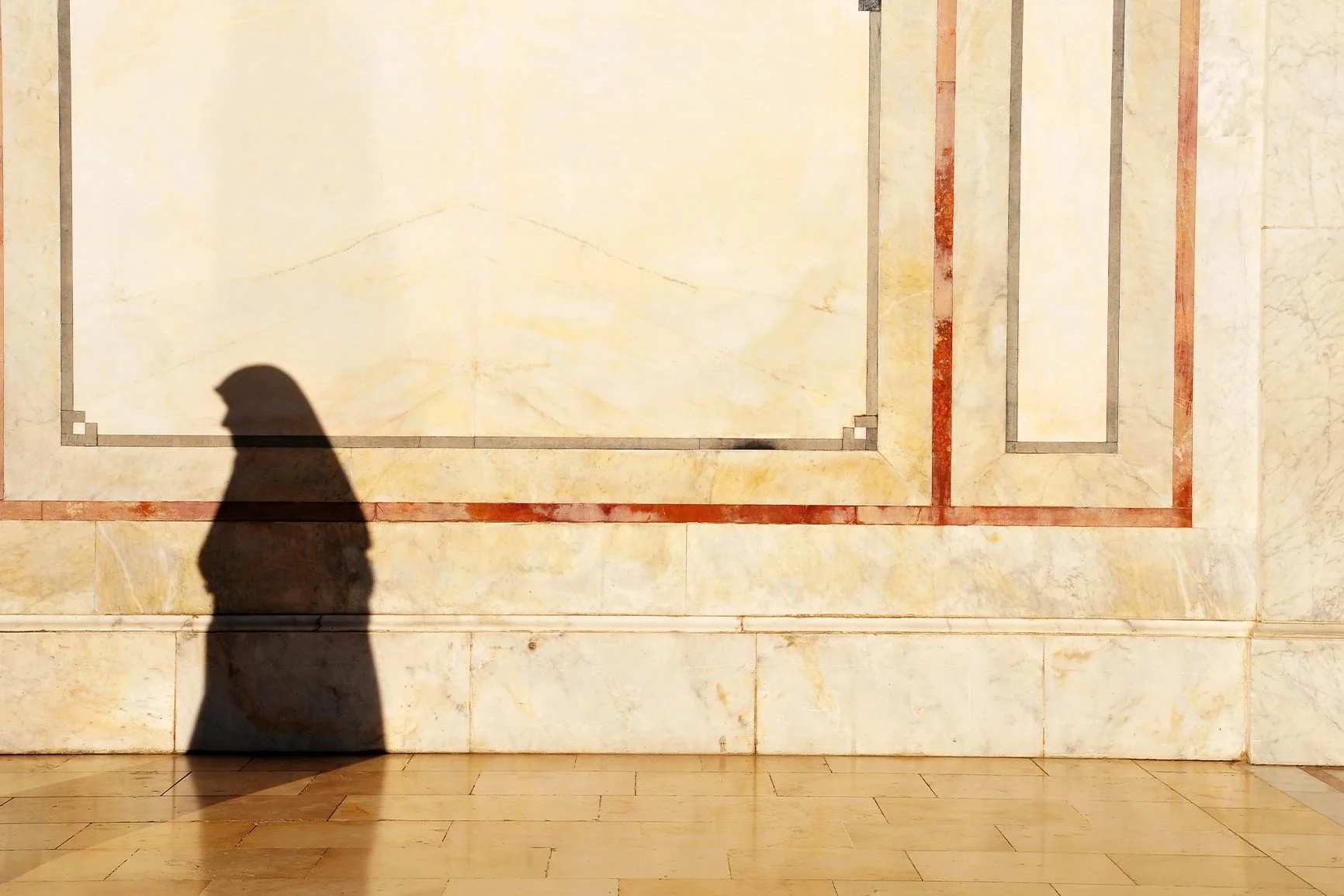 A person's shadow The shadow of a person wearing a headscarf against a light-colored wall with rectangular decorations.