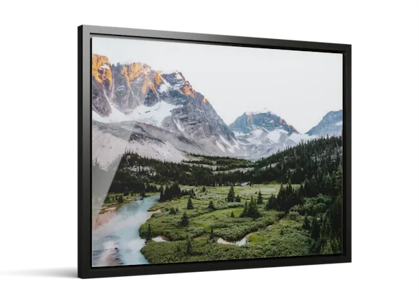 Framed photo print of a mountain landscape with snow-capped peaks, green valley, evergreen trees, and a winding turquoise river.