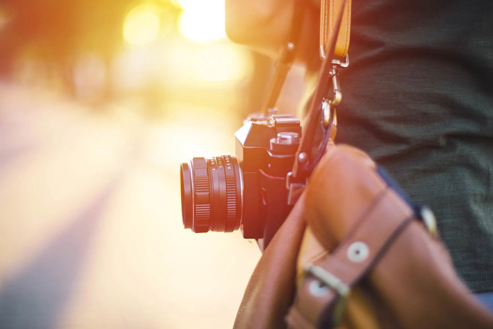 Camera on a strap A close-up of an analog camera hanging from a strap, with a blurred background and sunlight in the background.