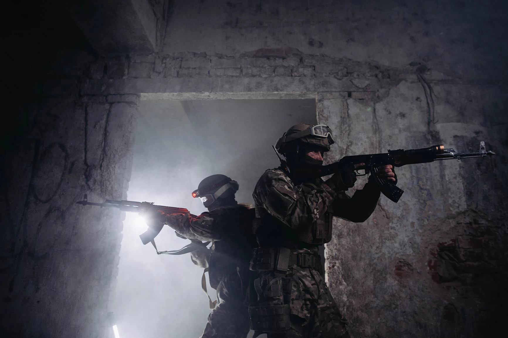 Armed soldiers in combat gear Two armed soldiers in combat gear are standing in a dark, dilapidated room, aiming their rifles.