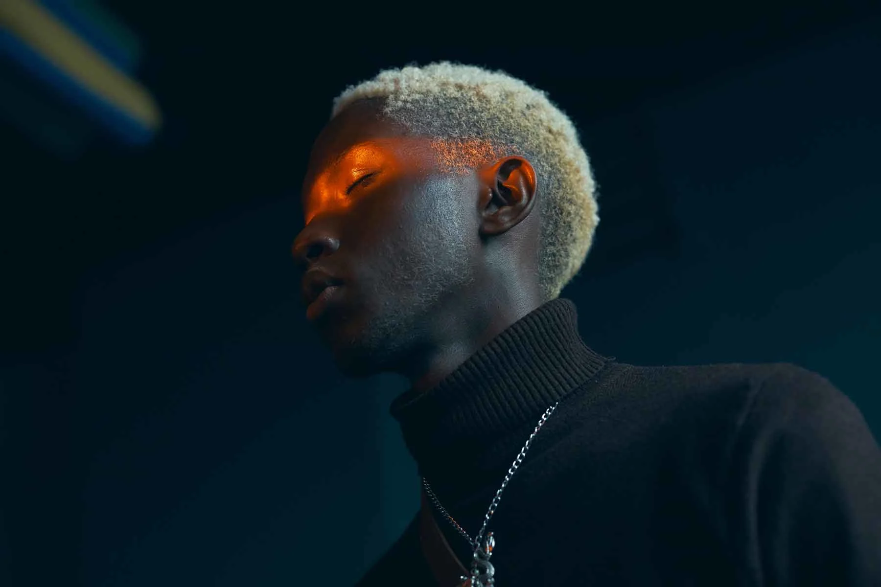 Retrato de un hombre de piel oscura con un jersey de cuello alto negro y rayas naranjas sobre los ojos. Retrato de un hombre de piel oscura con un jersey de cuello alto negro y rayas naranjas sobre los ojos.