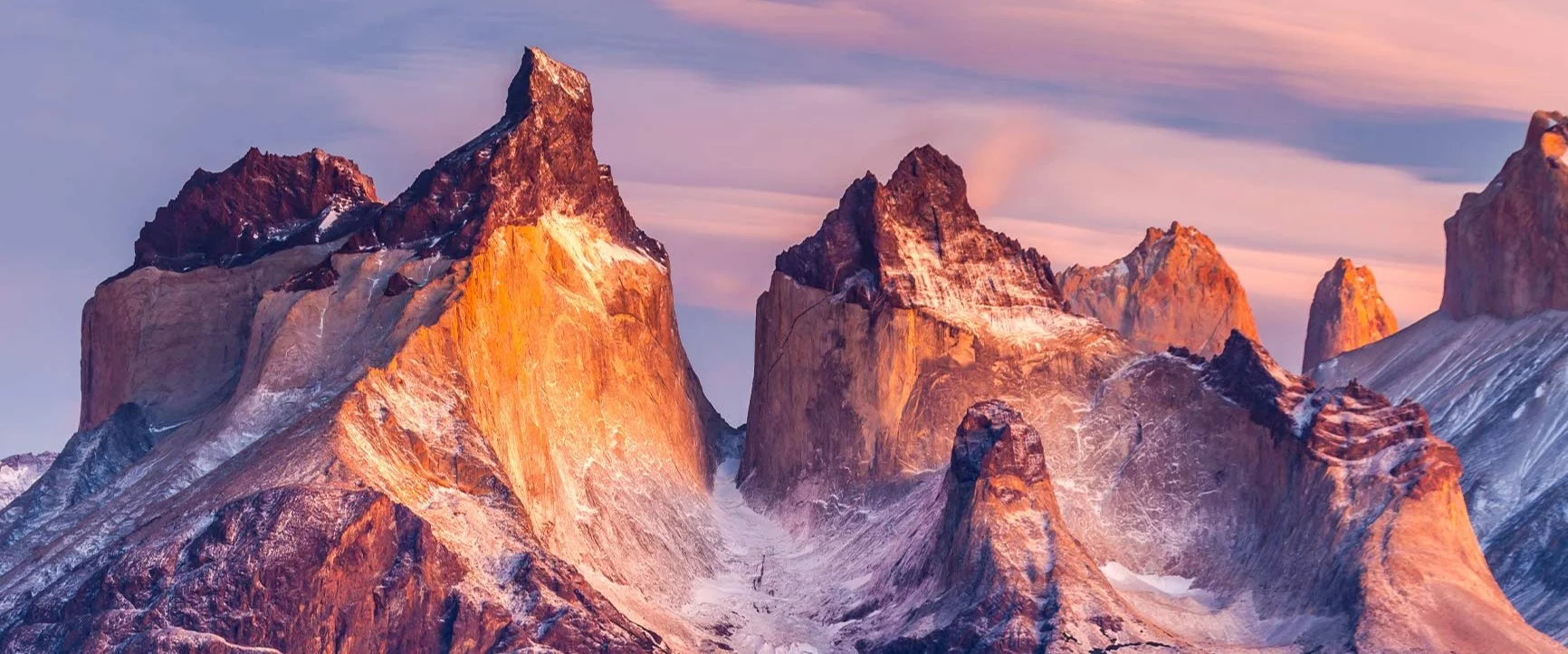 Rocky mountain peaks with snow-capped slopes beneath a pastel-colored sky.